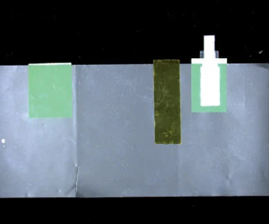 Source colour capture of a battery-cell face under a white bar light: two light-green films, one dark olive film and a white part at the upper edge. Complete capture, not retouched.