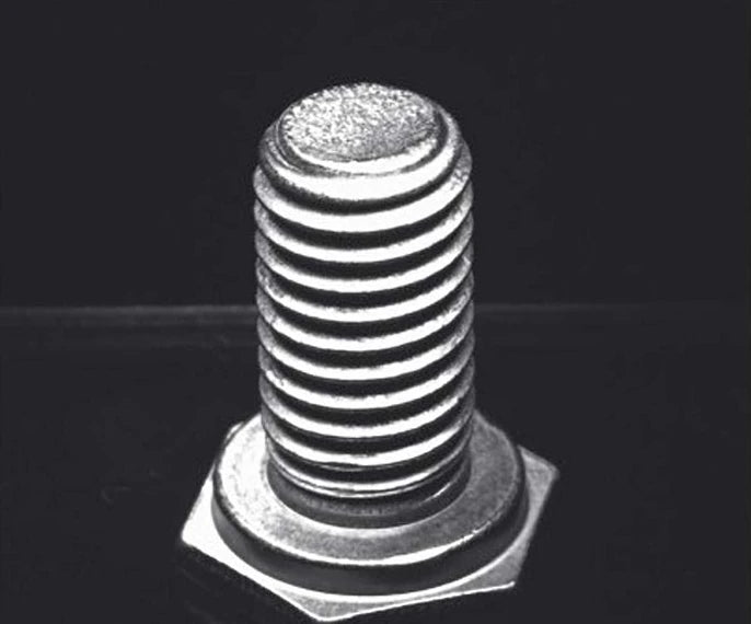 Source capture of a hex bolt standing on its head under a blue ring light: bright thread crests, dark roots and the end face on top. Complete capture inside the brochure frame, not retouched.