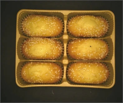Source colour capture of six seed-topped cakes in a tray under a white through-hole panel light. A small dark speck is visible on the middle-right cake. Complete capture, not retouched.