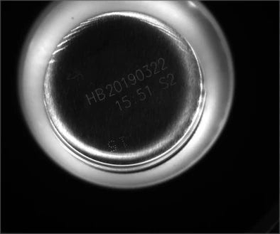Source capture of a can base under a 940 nm infrared ring light: a two-line printed date and time code on the domed metal end. Complete capture, not retouched.