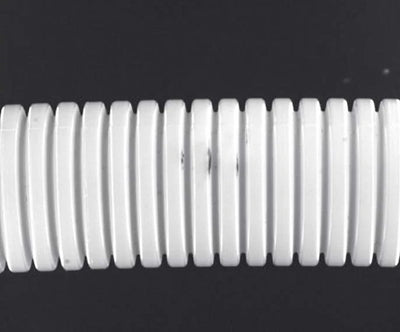 Source capture of a white corrugated hose under a white shadowless ring light: regular bright ribs with small dark marks on three neighbouring ribs. Complete capture inside the brochure frame, not retouched.