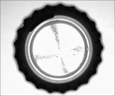 Source capture of the inside of a crown cap under a white polarized ring light: bright round liner with two dark crossing streaks of marks. Complete capture, not retouched.