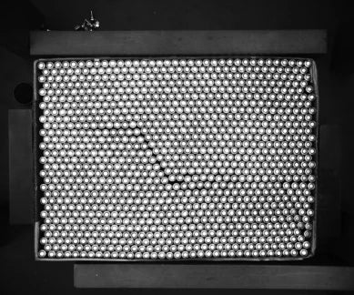 Source capture of a tray of cylindrical cells seen end-on under a white panel light: a dense pattern of bright cell ends with a diagonal line across it. Complete capture, not retouched.