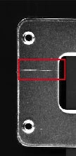 The source capture shows bright scratches on the dark metal cover; the red rectangle is the original test annotation. This crop excludes unrelated printed markings on the cover.