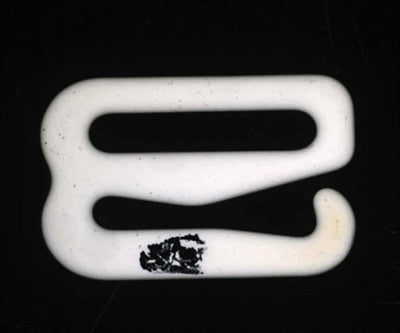 Source colour capture of a white moulded hook part under a white dome light: a dark dirt deposit on the lower bar. Complete capture inside the brochure frame, not retouched.