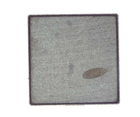 Source colour capture of a square inductor face under a white ring light: a brown smear near one corner of the grey face. Inside the brochure frame, not retouched.