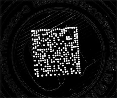Source trial A: a dotted two-dimensional code appears bright against the dark cap under UV illumination.