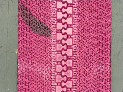 Source white-ring capture: interlocking zipper teeth and the adjacent pink fabric texture are visible. No slider or pull is demonstrated.