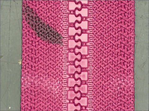 Source white-ring capture: interlocking zipper teeth and the adjacent pink fabric texture are visible. No slider or pull is demonstrated.